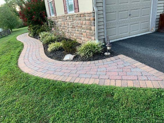 Curved brick pathway leading to a house with landscaped garden and greenery.