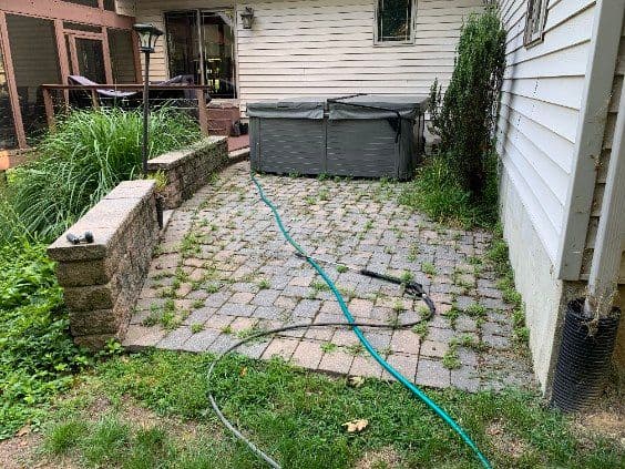 Paved patio area with a hot tub and garden hose beside a house.