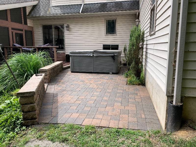 Paved patio area with a hot tub beside a house, featuring landscaping and seating.