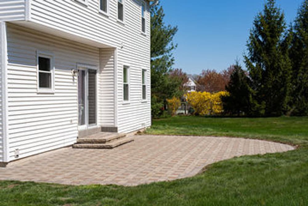 Patio with paver stones next to a modern white house and green lawn on a sunny day.