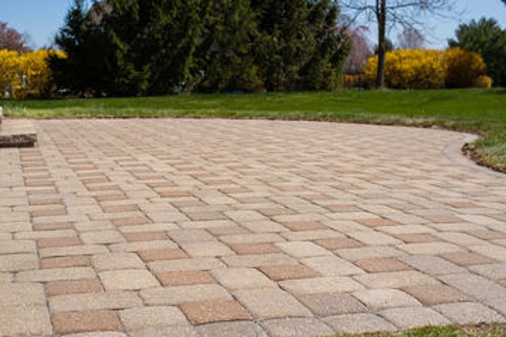 Patio area with paver stones beside a white house and lush green grass, sunny day scene.