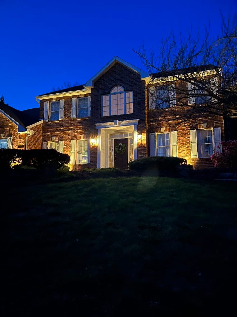 Elegant brick house illuminated at night with landscaped yard and decorative wreath on door.