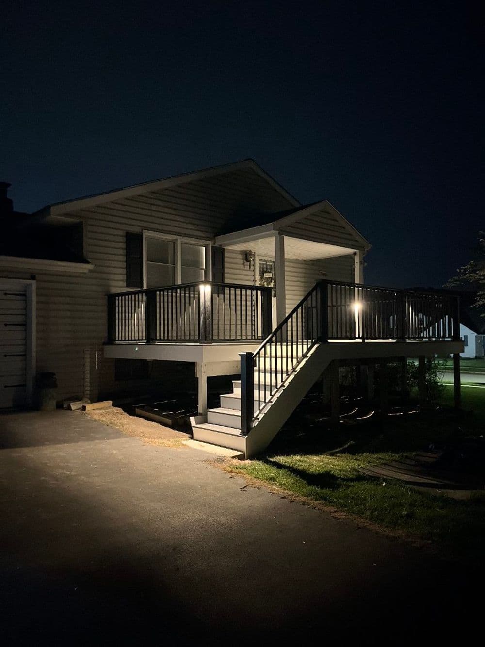 Well-lit house exterior at night featuring a deck, stairs, and driveway.
